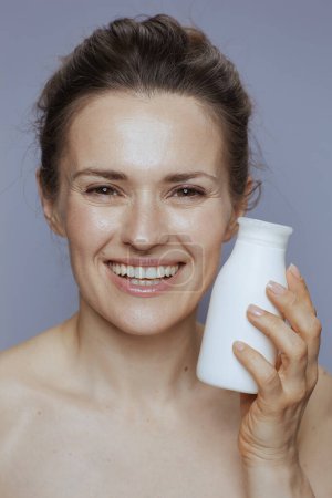 Photo for Portrait of smiling middle aged woman with cosmetic cream jar isolated on blue. - Royalty Free Image