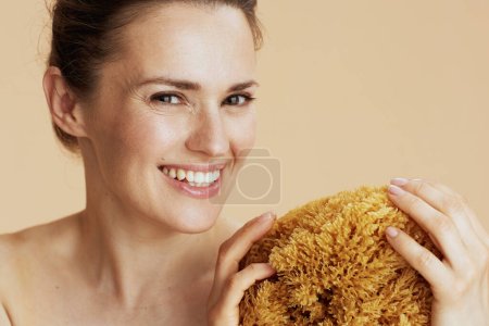 Foto de Sonriente mujer moderna con esponja de mar aislada en beige. - Imagen libre de derechos