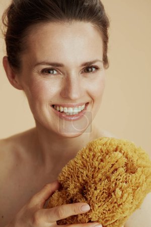 Foto de Retrato de una joven sonriente con esponja de mar sobre fondo beige. - Imagen libre de derechos