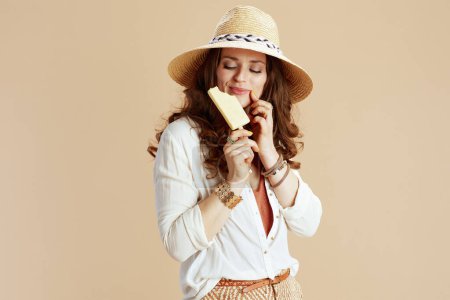 Photo for Beach vacation. happy modern 40 years old woman in white blouse and shorts against beige background with ice cream and straw hat. - Royalty Free Image