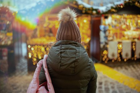 Foto de Visto desde atrás mujer con abrigo verde y sombrero marrón en la feria de invierno en la ciudad. - Imagen libre de derechos