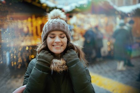 Photo for Relaxed modern female in green coat and brown hat at the winter fair in the city. - Royalty Free Image