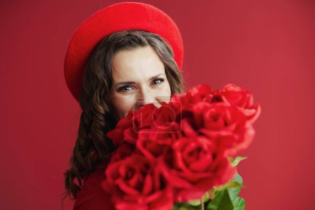 Téléchargez les photos : Joyeux Valentin. élégante femme de 40 ans en robe rouge et béret sur fond rouge avec des roses rouges. - en image libre de droit