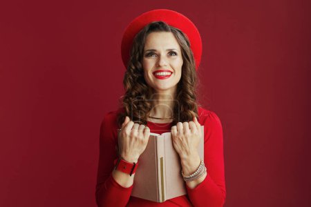Photo for Happy Valentine. smiling elegant female with long wavy hair in red dress and beret against red background with book. - Royalty Free Image