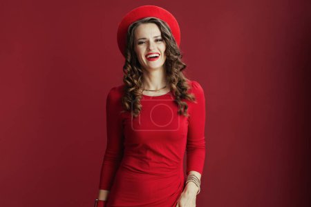 Téléchargez les photos : Joyeux Valentin. Portrait de heureuse femme élégante de 40 ans avec de longs cheveux ondulés en robe rouge et béret sur fond rouge. - en image libre de droit