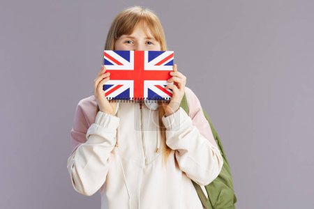 modern pupil in beige tracksuit with backpack and english flag workbook isolated on grey background.