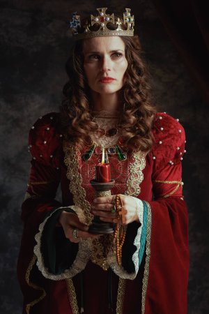 Foto de Reina medieval en vestido rojo con vela y corona sobre fondo gris oscuro. - Imagen libre de derechos