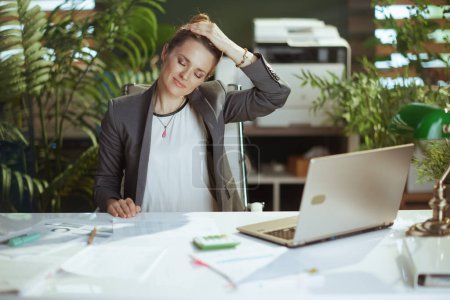 Téléchargez les photos : Un lieu de travail durable. souriant femme d'affaires moderne au travail avec ordinateur portable étirant cou. - en image libre de droit