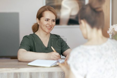 Photo for Healthcare time. smiling female medical massage therapist in massage cabinet with client and notebook on reception. - Royalty Free Image