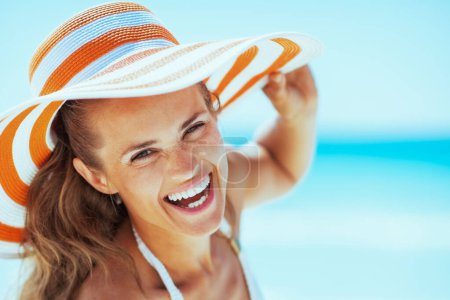 Téléchargez les photos : Jeune femme souriante en maillot de bain et chapeau de plage au bord de la mer - en image libre de droit