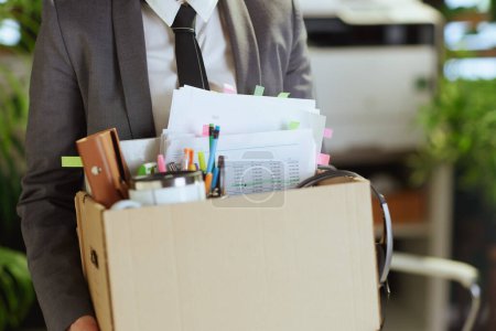 Photo for New job. Closeup on modern 40 years old woman employee in modern green office in grey business suit with personal belongings in cardboard box. - Royalty Free Image