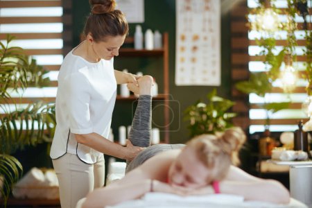 Photo for Healthcare time. female medical massage therapist in massage cabinet with teenage client making massage on massage table. - Royalty Free Image