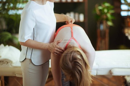 Photo for Healthcare time. female medical massage therapist in massage cabinet with teenage client checking clients back condition during examination. - Royalty Free Image