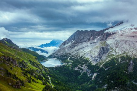 Foto de Hora de verano en Dolomitas. paisaje con montañas, colinas, lago Fedaia, nubes y bosque. - Imagen libre de derechos