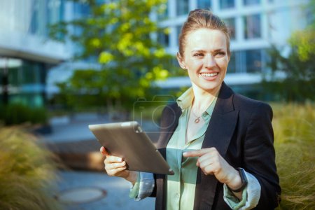 Foto de Feliz moderno 40 años de edad, mujer trabajadora cerca de edificio de oficinas en chaqueta negra con tableta digital. - Imagen libre de derechos