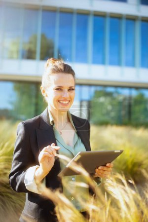 Foto de Sonriente empleada moderna en el distrito de negocios en chaqueta negra con tablet PC. - Imagen libre de derechos