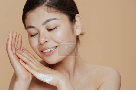 Téléchargez les photos : Portrait de jeune femme avec crème pour les mains sur fond beige. - en image libre de droit