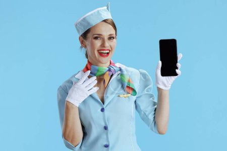 Photo for Smiling elegant stewardess woman isolated on blue background in blue uniform showing smartphone blank screen. - Royalty Free Image