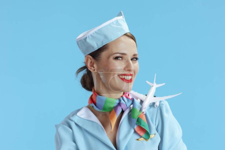 Foto de Mujer azafata moderna sonriente aislada sobre fondo azul en uniforme azul con un pequeño avión. - Imagen libre de derechos