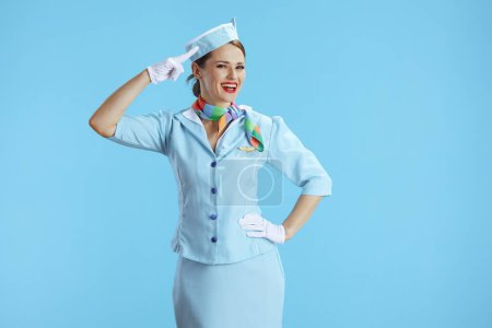 Foto de Sonriente elegante azafata de aire femenino sobre fondo azul en azul uniforme saludos. - Imagen libre de derechos