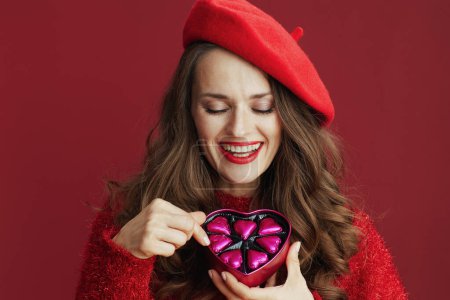 Téléchargez les photos : Joyeux Valentin. heureux élégant femelle en pull rouge et béret avec boîte de bonbons en forme de coeur. - en image libre de droit