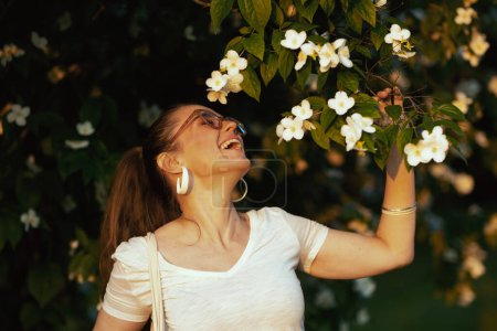 Foto de Hora de verano. feliz mujer elegante en camisa blanca con anteojos cerca del árbol de la floración. - Imagen libre de derechos