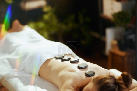 Photo for Healthcare time. relaxed modern 40 years old woman in spa salon having hot stone massage and laying on massage table. - Royalty Free Image