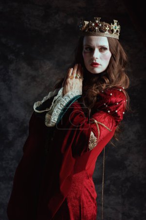 Foto de Reina medieval en vestido rojo con maquillaje blanco y corona sobre fondo gris oscuro. - Imagen libre de derechos