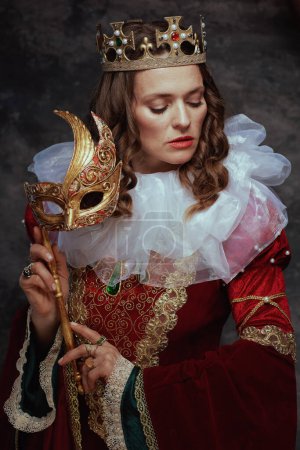 Foto de Reina medieval en vestido rojo con máscara veneciana, cuello blanco y corona sobre fondo gris oscuro. - Imagen libre de derechos
