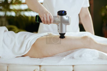 Photo for Healthcare time. Closeup on massage therapist in massage cabinet with massage pistol massaging clients leg. - Royalty Free Image