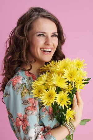 Téléchargez les photos : Femme moderne souriante en robe florale avec des fleurs de chrysanthèmes jaunes isolées sur rose. - en image libre de droit