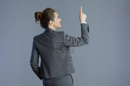 Foto de Visto desde atrás mujer trabajadora en traje gris apuntando hacia arriba aislado sobre gris. - Imagen libre de derechos