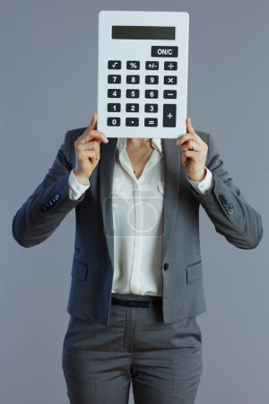 Téléchargez les photos : Élégante travailleuse de 40 ans en costume gris avec calculatrice isolée sur fond gris. - en image libre de droit