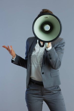 Téléchargez les photos : Élégante propriétaire de petite entreprise d'âge moyen femme en costume gris avec mégaphone isolé sur gris. - en image libre de droit