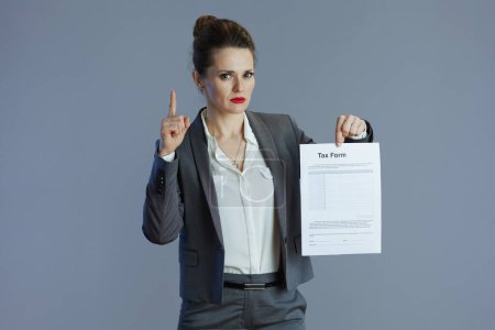Téléchargez les photos : Élégant 40 ans femme employée en costume gris avec formulaire d'impôt isolé sur gris. - en image libre de droit