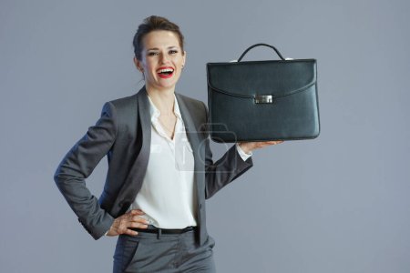 Photo for Smiling elegant small business owner woman in grey suit with briefcase against gray background. - Royalty Free Image