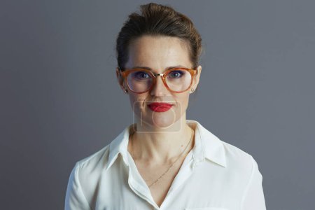 Téléchargez les photos : Élégante femme propriétaire de petite entreprise d'âge moyen en chemisier blanc avec des lunettes isolées sur gris. - en image libre de droit
