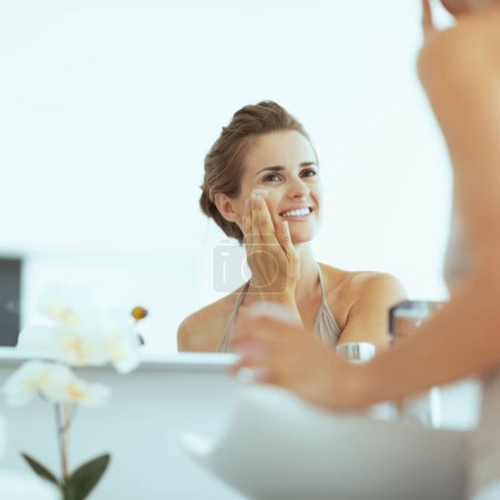 Photo for Happy young woman applying cream in bathroom - Royalty Free Image