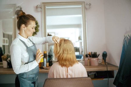 Foto de Peluquería femenina en el moderno salón de belleza con spray para el cabello y cliente. - Imagen libre de derechos