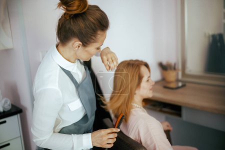 Foto de 40 años de edad empleado de peluquería en estudio de pelo moderno con cepillo de pelo y cliente. - Imagen libre de derechos