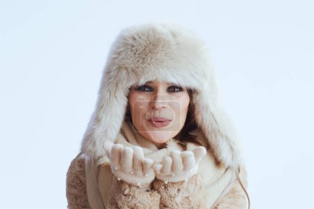 Foto de Feliz elegante mujer de 40 años en abrigo de invierno y sombrero de piel aislado sobre fondo blanco en guantes blancos soplado beso. - Imagen libre de derechos