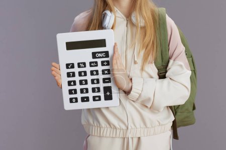 Photo for Closeup on school girl in beige tracksuit with backpack, calculator and headphones isolated on grey. - Royalty Free Image