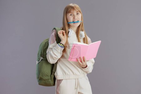 Téléchargez les photos : Portrait d'adolescente tendance souriante en survêtement beige avec sac à dos, classeurs, écouteurs et stylo isolés sur fond gris. - en image libre de droit