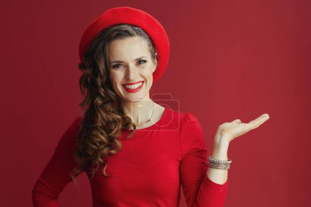 Photo for Happy Valentine. Portrait of smiling elegant 40 years old woman with long wavy hair in red dress and beret against red background. - Royalty Free Image