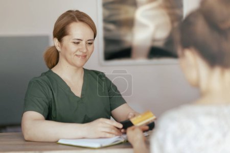 Téléchargez les photos : Temps de santé. heureuse massothérapeute femme dans l'armoire de massage avec client acceptant les paiements par carte de crédit via terminal à la réception. - en image libre de droit
