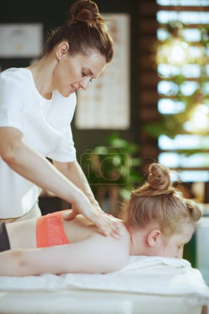 Téléchargez les photos : Temps de santé. Massothérapeute médicale féminine dans une armoire de massage avec un client adolescent faisant un massage sur une table de massage. - en image libre de droit