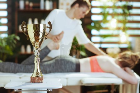 Photo for Healthcare time. Closeup on massage therapist woman in massage cabinet with clipboard, teenage client and award cup making massage. - Royalty Free Image