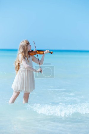 Photo for Modern young woman in light dress on the ocean coast with violin enjoying playing. - Royalty Free Image