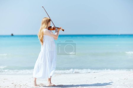 Téléchargez les photos : Portrait complet de jeune femme moderne en robe blanche avec violon jouant sur la plage. - en image libre de droit