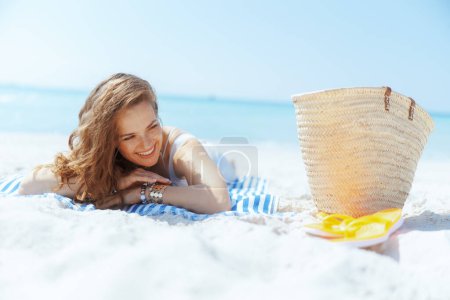 Photo for Happy stylish woman on the ocean coast with straw bag and striped towel. - Royalty Free Image